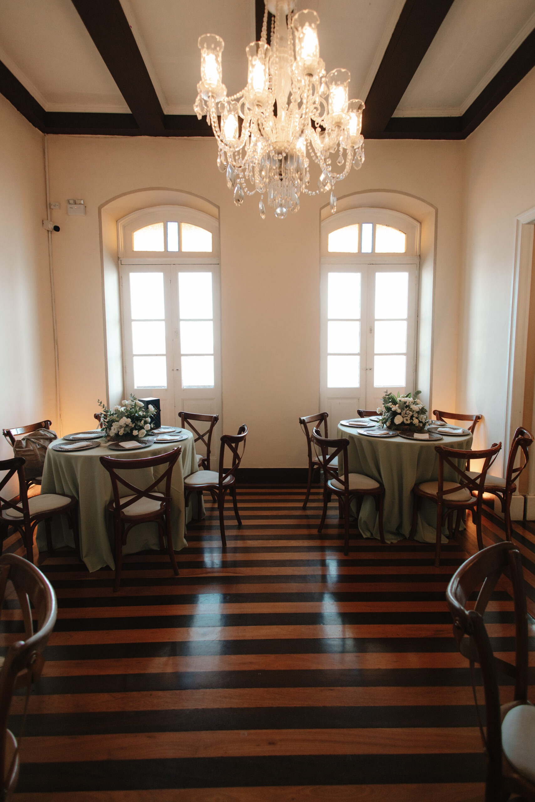 Ambiente interno com mesas preparadas, lustre e decoração elegante.